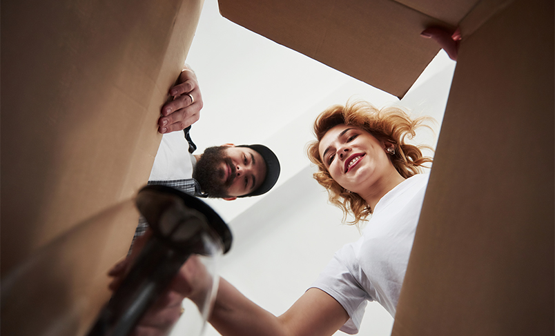 Uśmiechnięta para pakująca rzeczy w&nbsp;kartony do&nbsp;przeprowadzki w&nbsp;Andrychowie, symbolizująca bezstresowe przeprowadzki mieszkań i&nbsp;profesjonalne zabezpieczenie mienia.