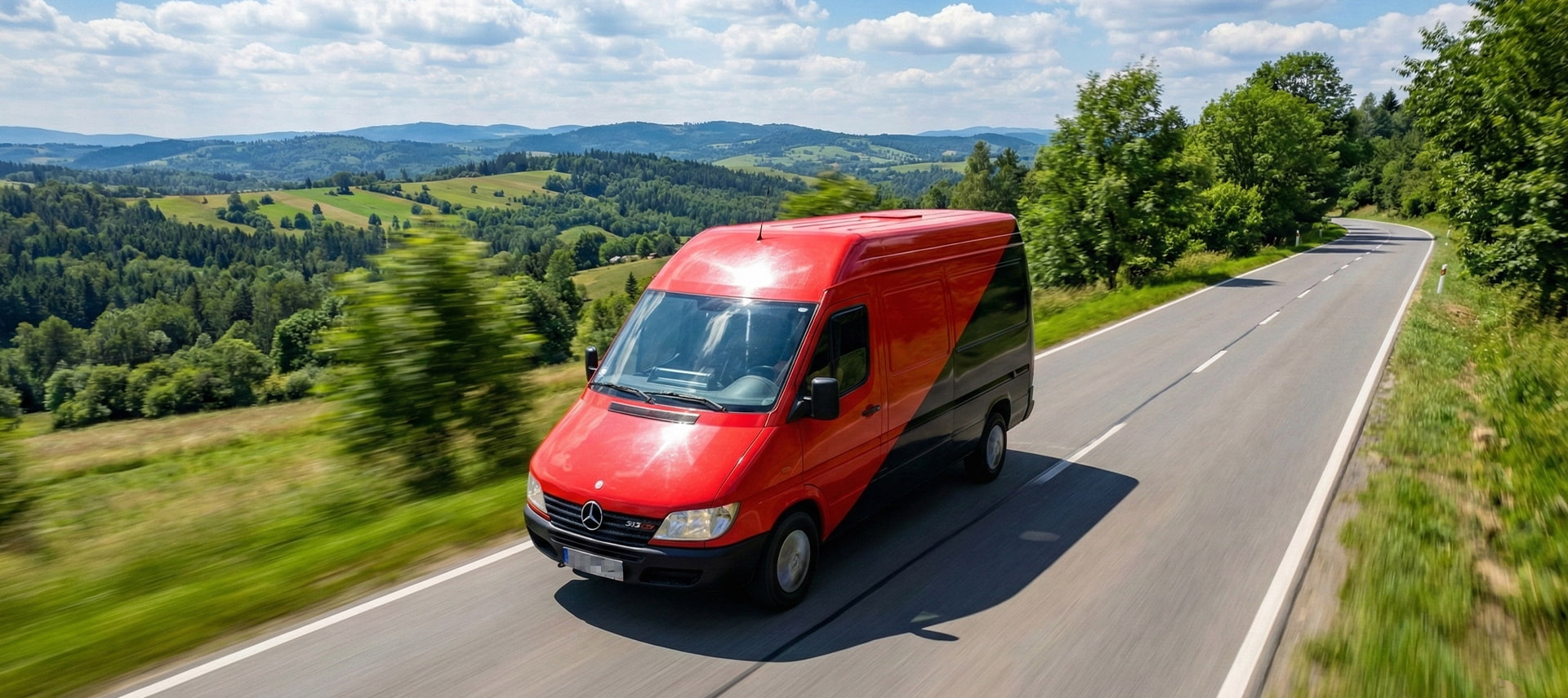 Czerwono-czarny furgon Boxperto Andrychów&nbsp;jadący przez zielone, pagórkowate tereny, realizujący bezpieczny transport mienia w&nbsp;ramach przeprowadzek krajowych.